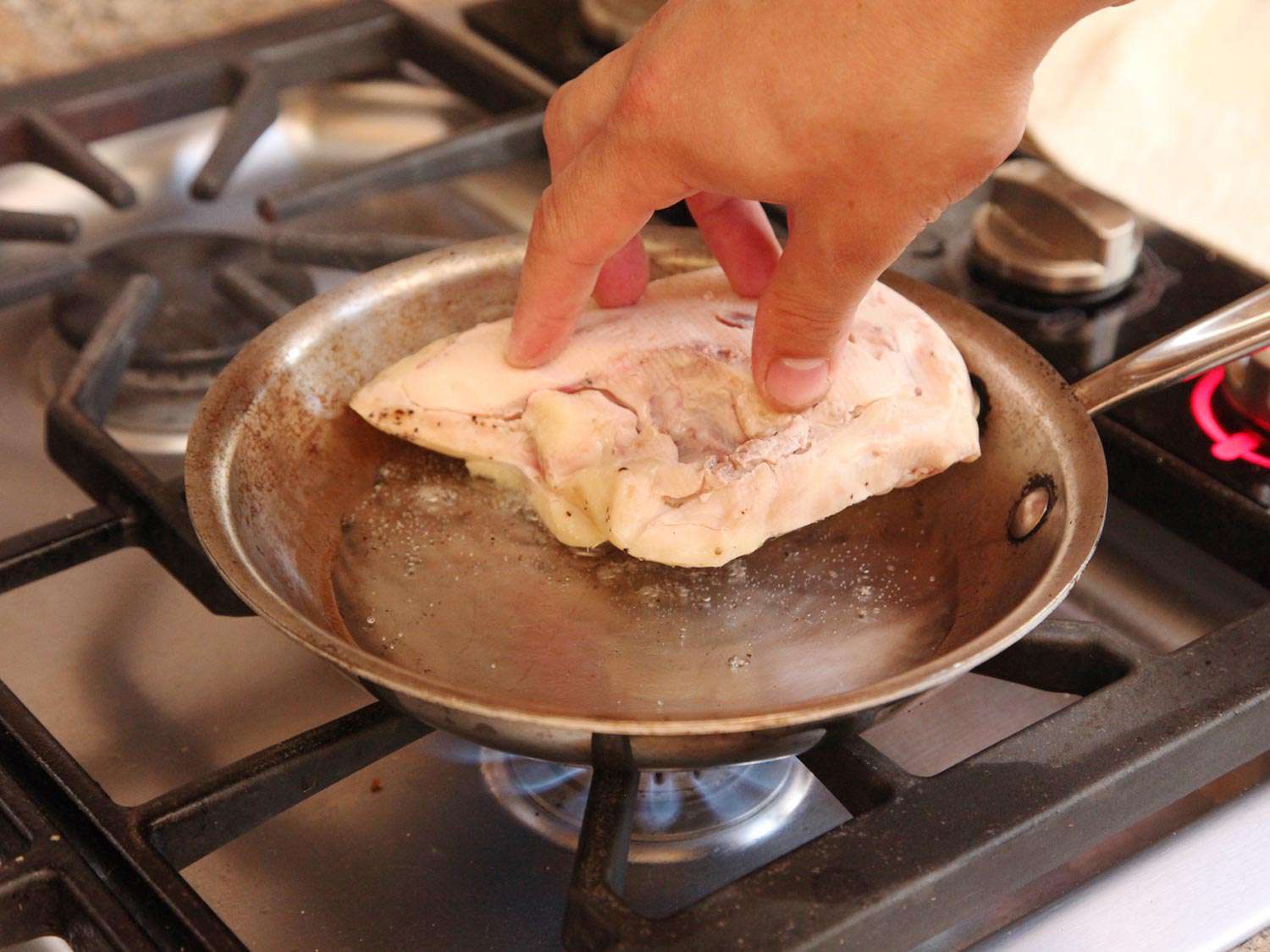 Pressing sous vide cooked chicken breast into a skillet on the stovetop.