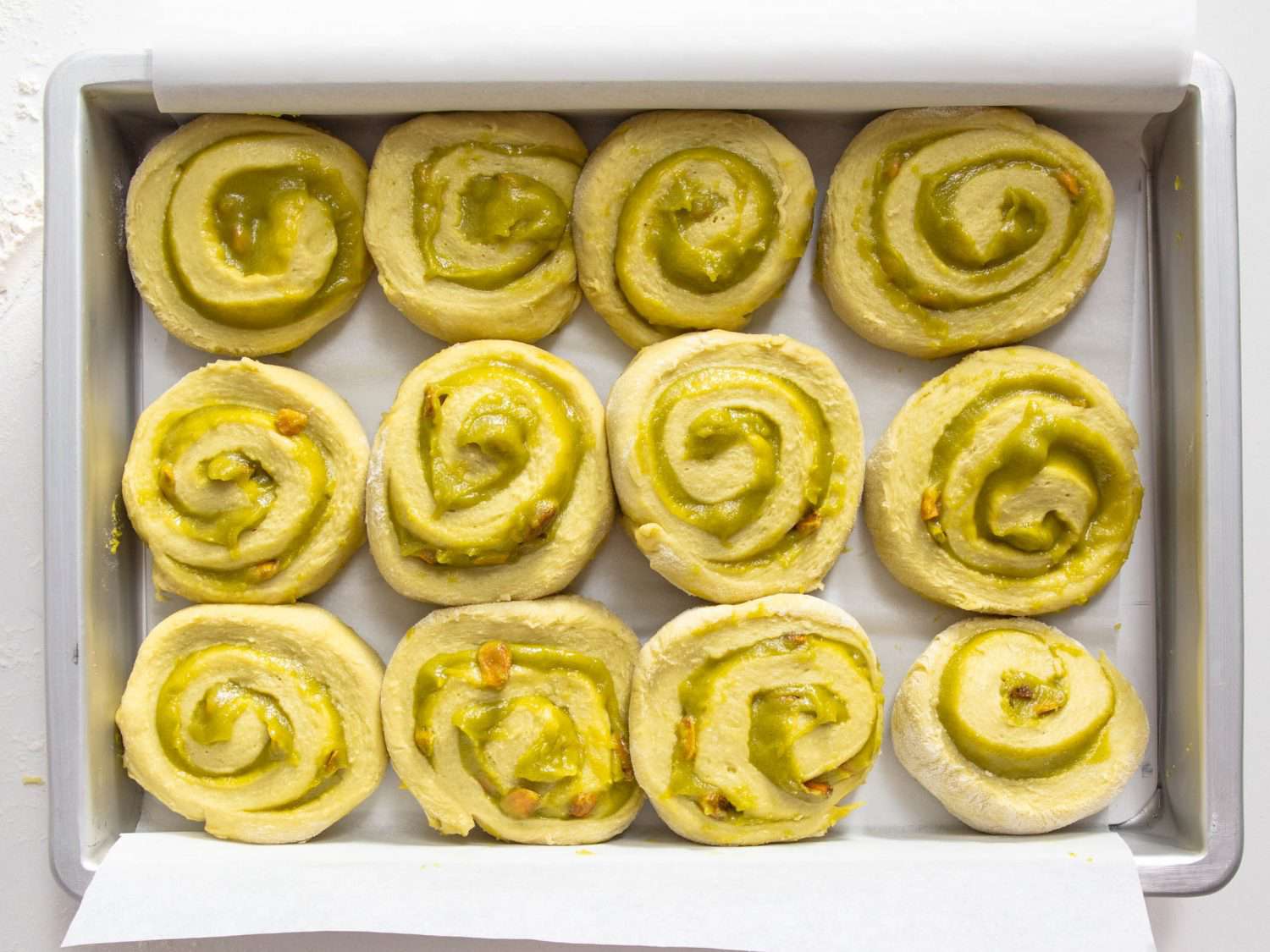 Raw pistachio buns arranged in a pan.
