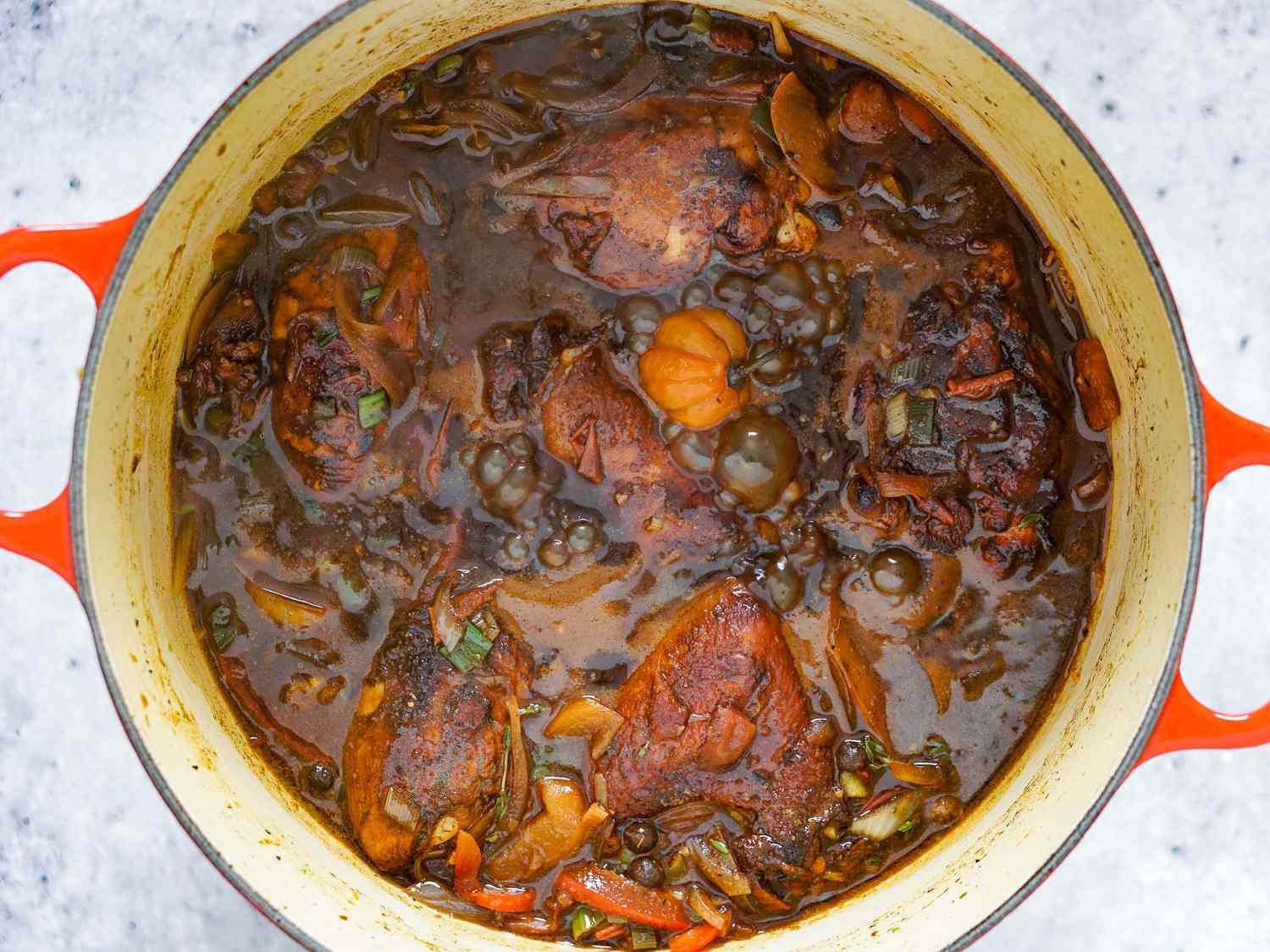 Dark chicken meat portions tucked into brown stew chicken stewing liquid