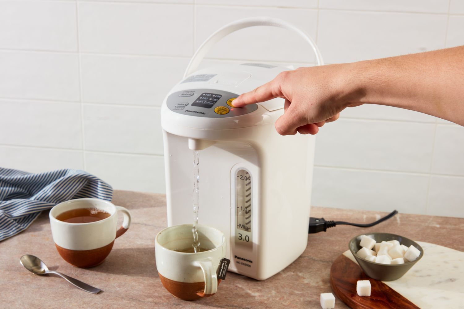A person dispensing water into a cup with a hot water dispenser.