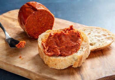 'Nduja next to a slice of bread slathered with 'nduja and a knife on a wooden block.