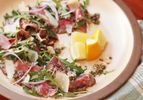 Closeup of steak carpaccio salad, served with a quartered lemon half.