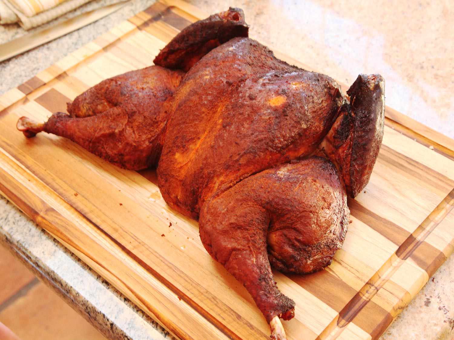 Butterflied, smoked turkey on a cutting board, legs splayed outward, ready to be carved.