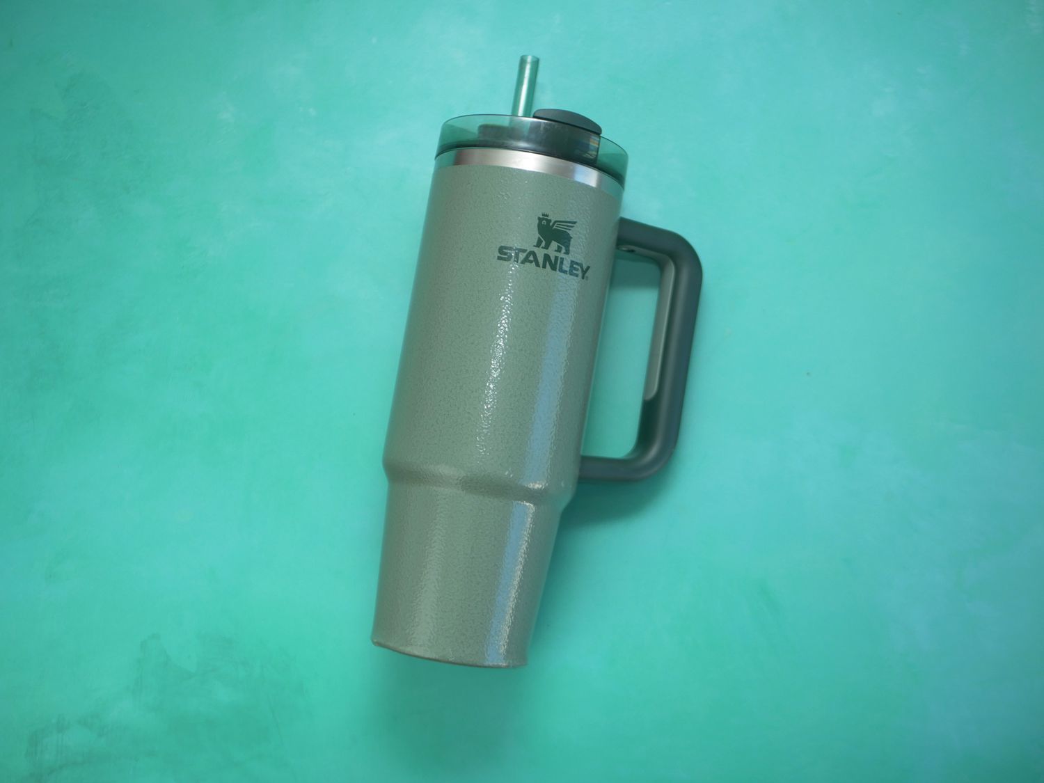 a green stanley tumbler on a blue green surface