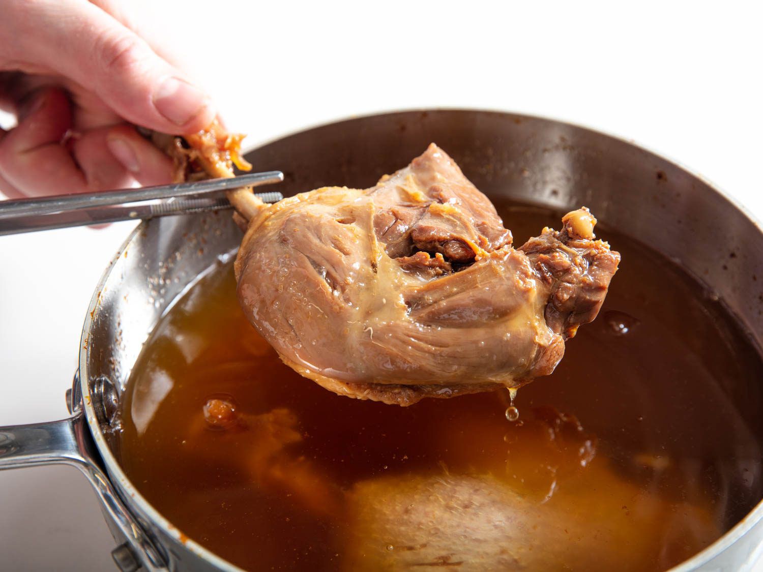 Pulling a leg of koji duck confit out of a saucepan.