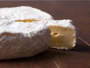 A wheel of brie cheese with a slice cut and slightly pulled away to show the creamy interior.