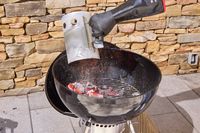 A hand adding hot coals to the Weber Original Kettle Premium 22-Inch Charcoal Grill