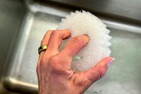 A hand holding the Scrub Daddy dishwashing sponge over a kitchen sink