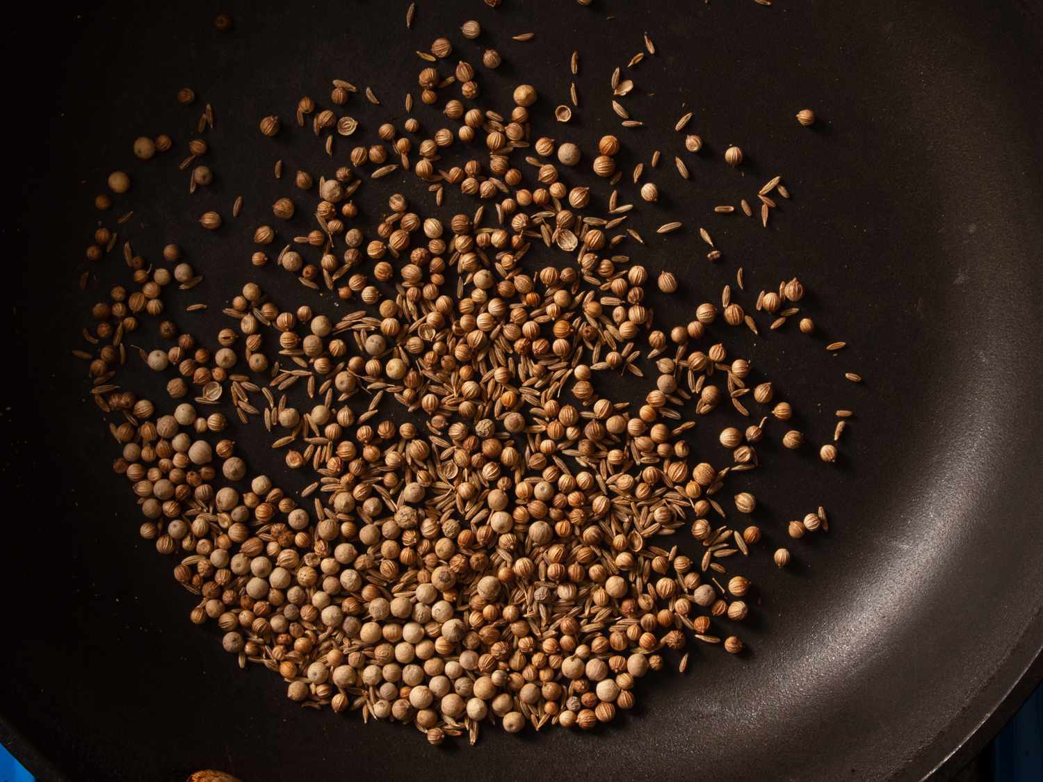 coriander, cumin, and white peppercorns toasting in skillet