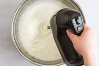 A person using a hand mixer to make whipped cream.