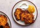 Three crispy sweet potato latkes on a ceramic plate alongside apple sauce and sour cream.
