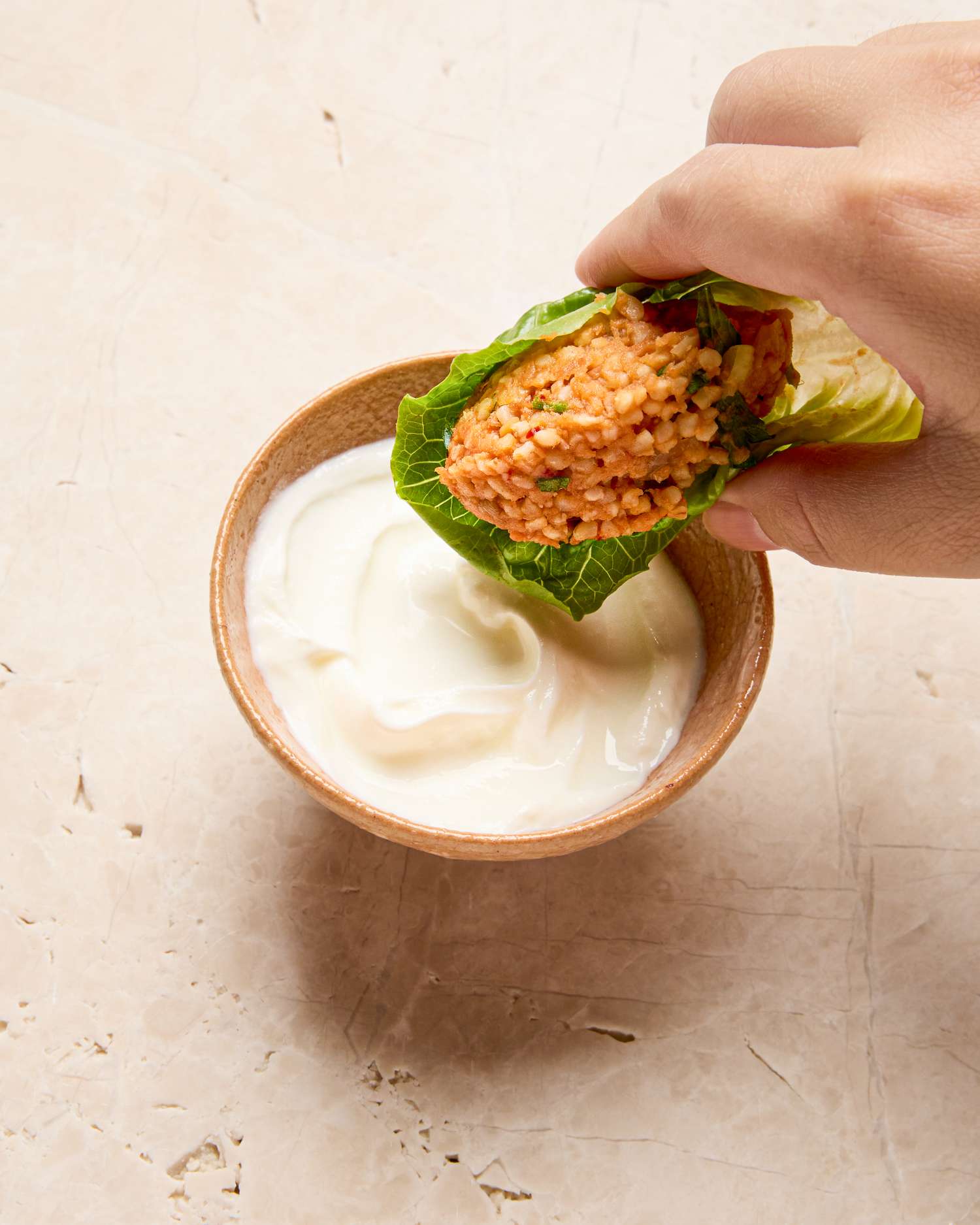 A hand holding a wrap above a bowl of yogurt or sauce