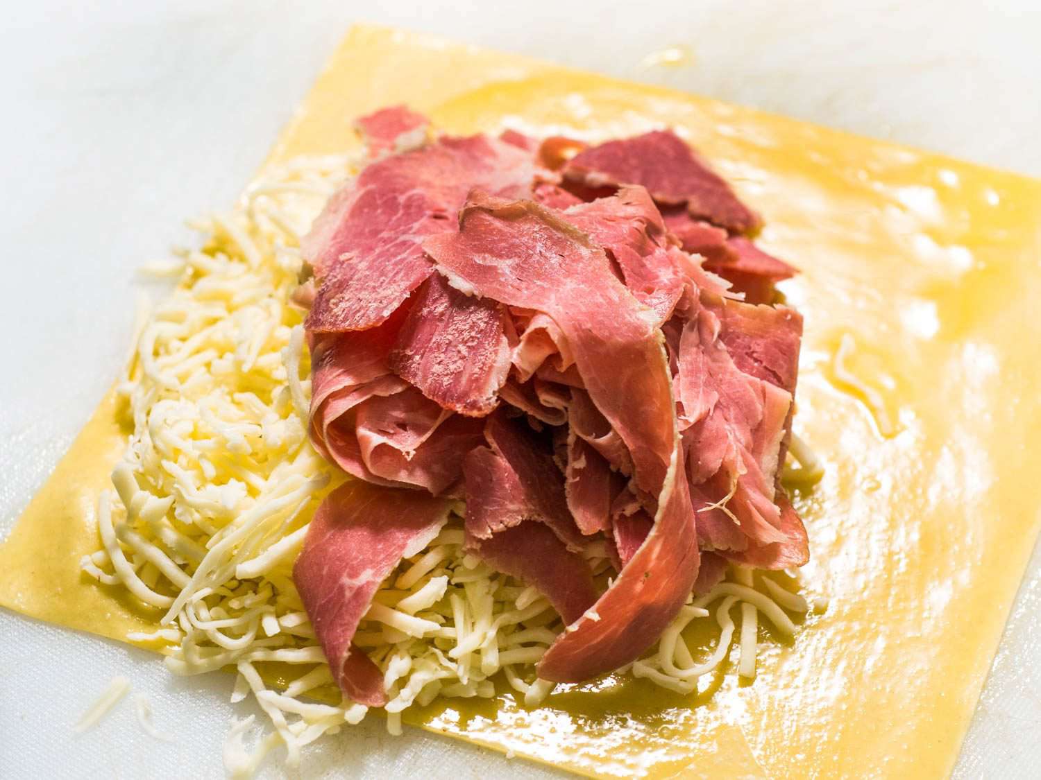 Corned beef on top of cheese, cabbage, and an egg roll wrapper, uncooked.