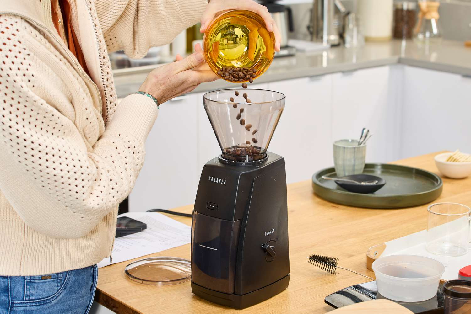 A person adding coffee beans to the Baratza Encore grinder's hopper.