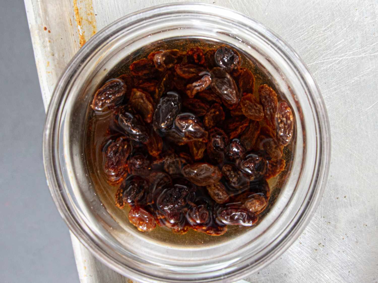 A jar containing brown liquid with soaked raisins floating inside placed on a metal surface