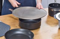 a person putting a splatter screen on a shallow pot
