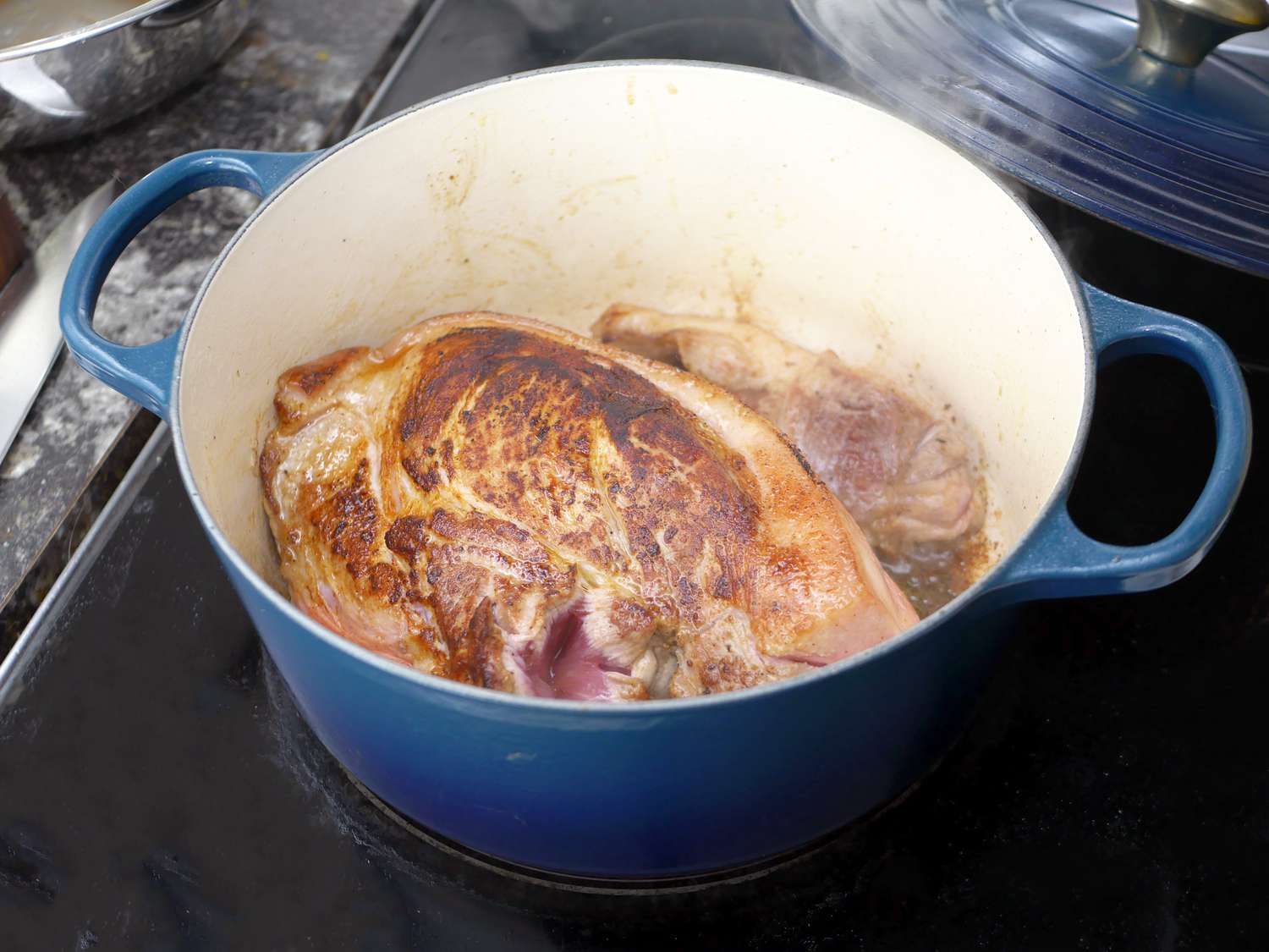 the le creuset dutch oven with seared pork shoulder inside, showing the fond development on the creamy enamel 