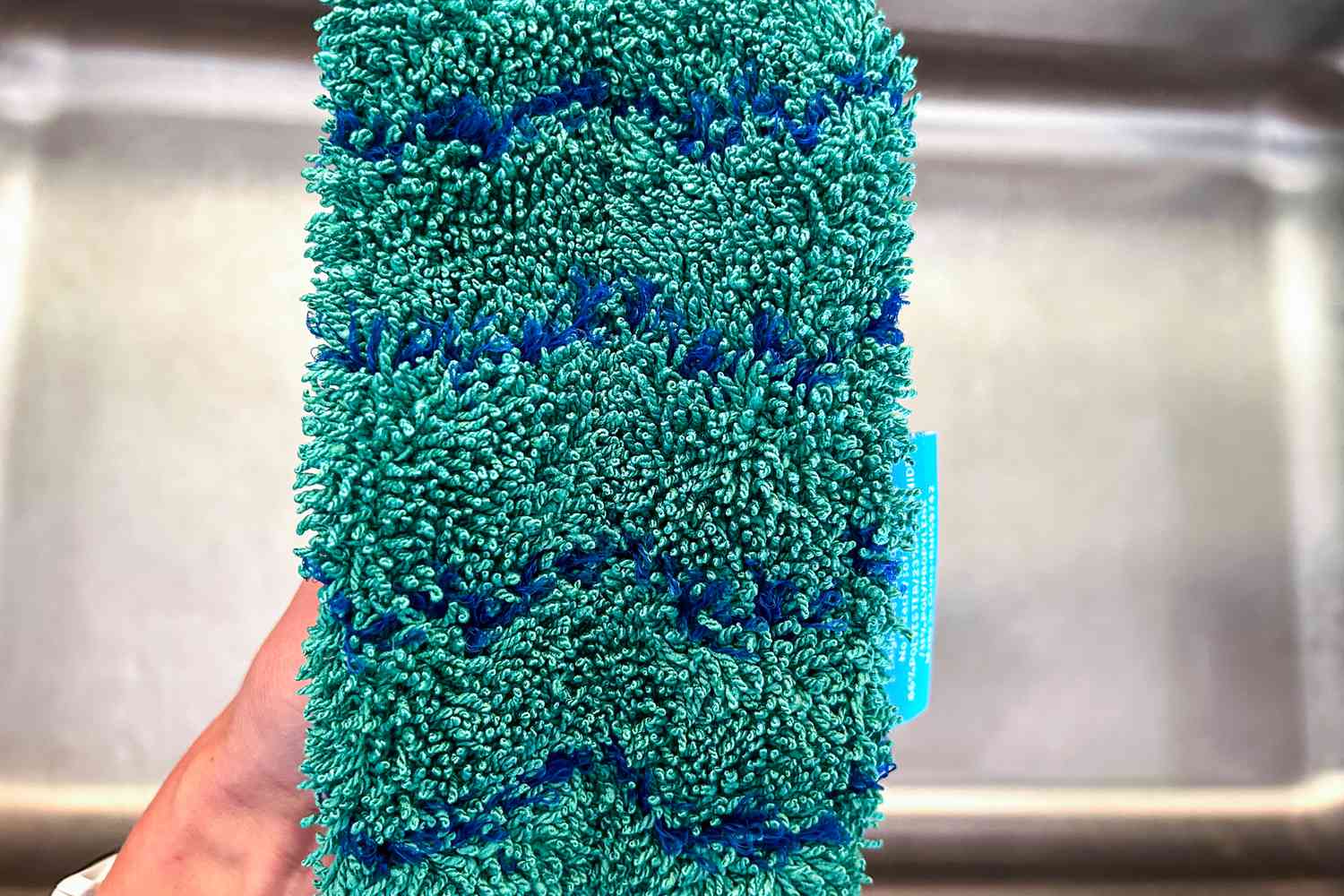 A hand holding a microfiber dishwashing sponge.