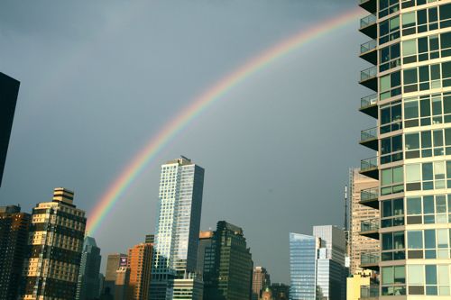A full rainbow stretching across the skyline view from a New York city rooftop.