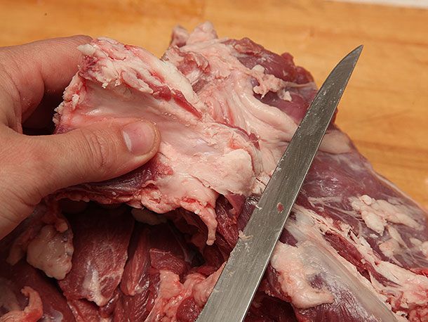 Removing interior fat from lamb leg with a boning knife.