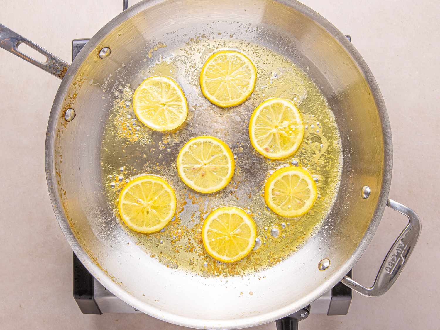 Lemon slices being sauted in a stainless steel skillet on a stove