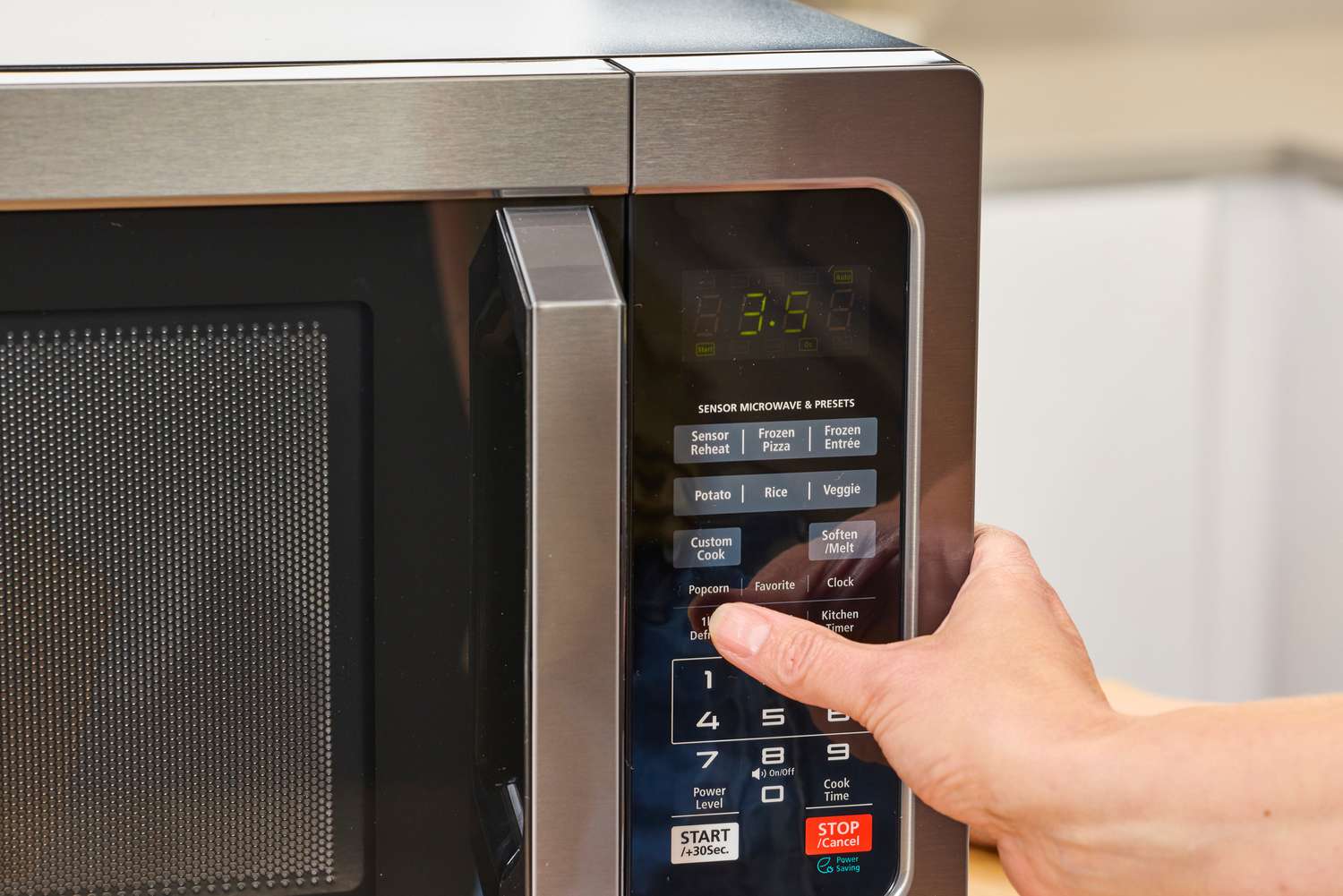 A thumb pressing a button on the Toshiba EM131A5C-BS Microwave Oven