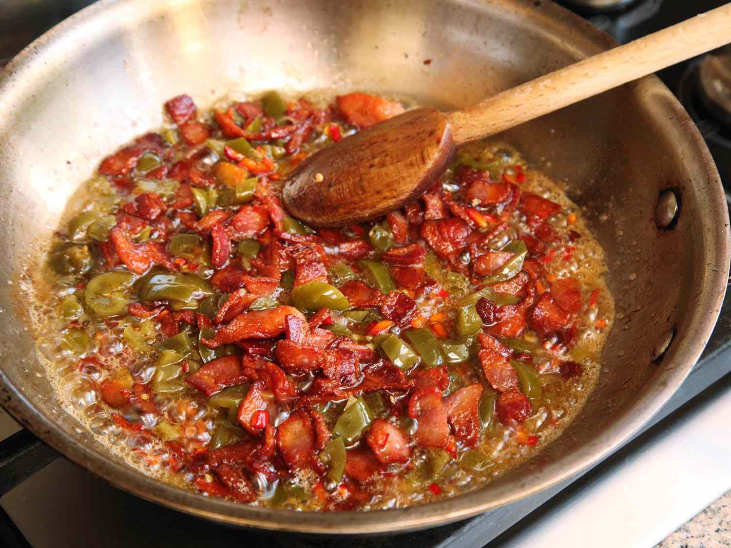 Bacon and jalapenos are cooked in a skillet.