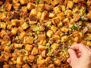 Hand adjusting pieces of bread stuffing mixed with herbs and vegetables