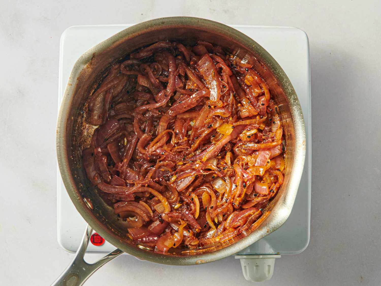 A saucepan filled with sauted onions on a portable hotplate