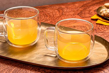 A metal tray with two ginger hot toddies served in glass mugs with lemon slices
