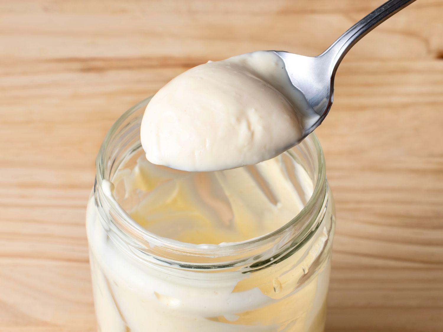 Fully emulsified mayonnaise on a spoon, above the glass jar it was emulsified in.