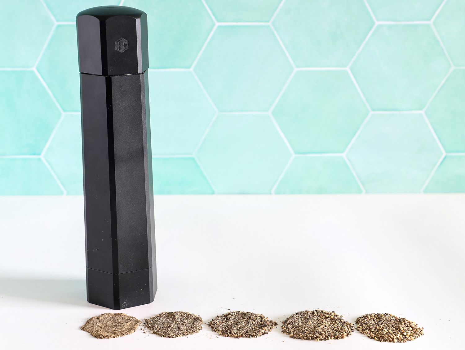 The HexClad HexMill Pepper Grinder in front of ground spices
