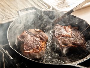 Two steaks cooking in a cast iron skillet with steam rising up