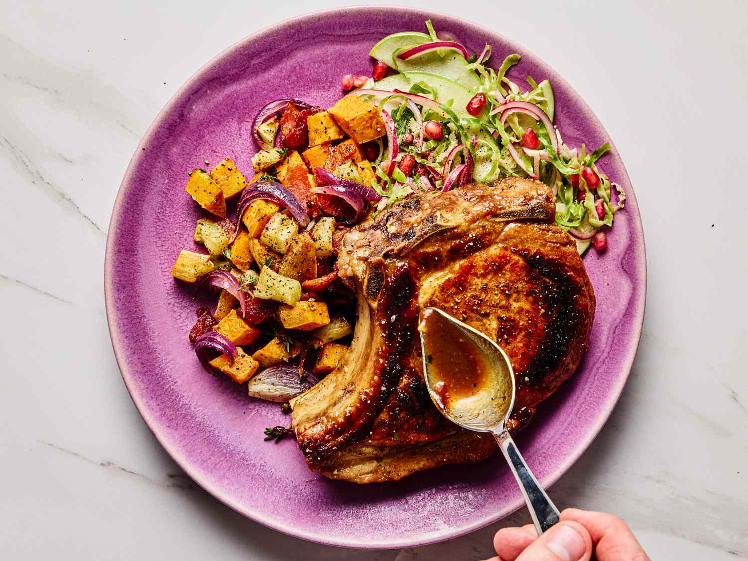 Plate with apple butter glazed pork chops roasted vegetables and a side salad with a hand spooning glaze over the meat