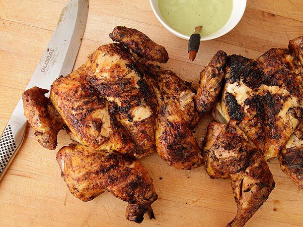 Grilled Peruvian-style chickens on a cutting board next to green sauce.
