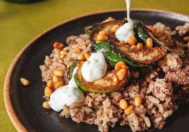 A dish with stuffed zucchini rice and yogurt sauce being poured on top garnished with pine nuts
