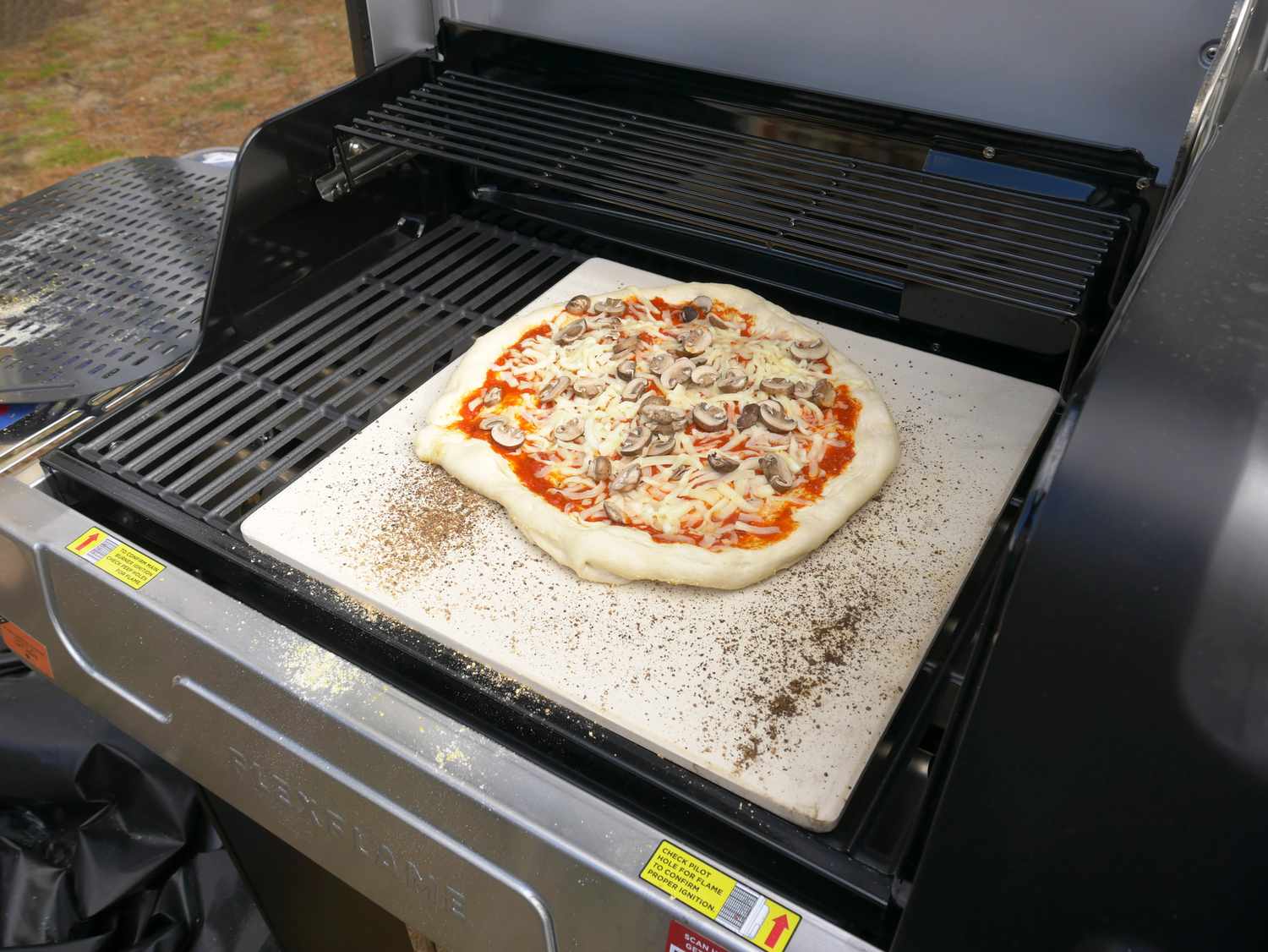 a pizza cooking on a pizza stone in a grill