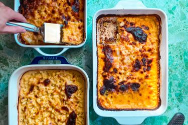 Three rectangular baking dishes of baked macaroni and cheese one with a slice being lifted with a spatula