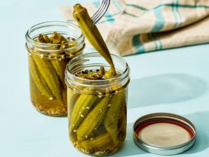 Two jars of pickled okra one jar with a fork lifting a piece of okra