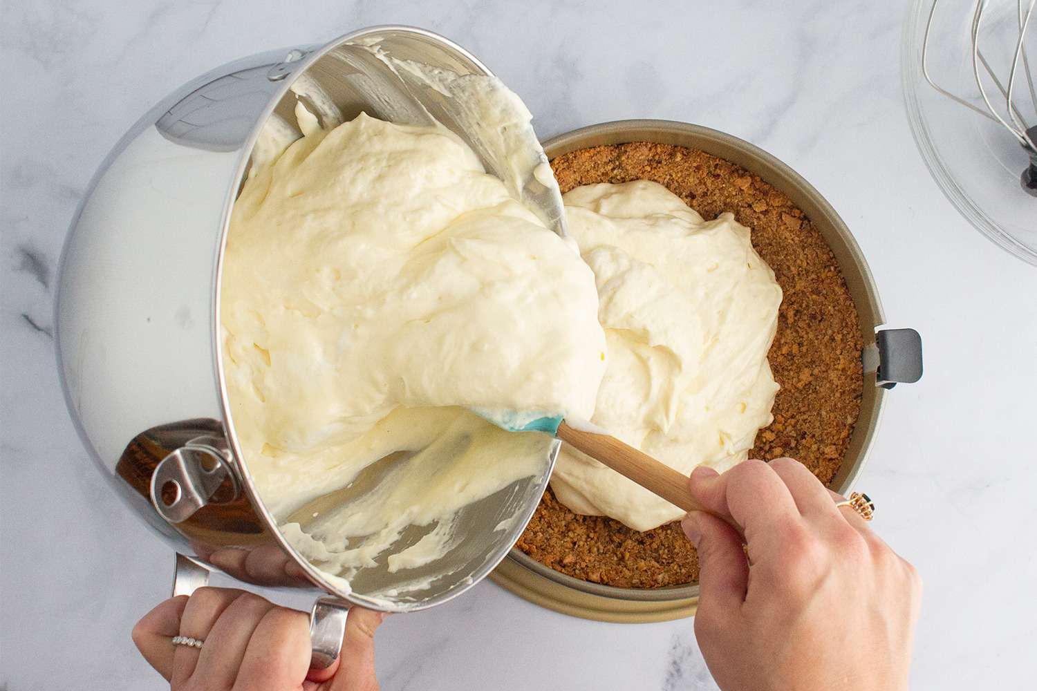 A person pouring cheesecake batter from a bowl into a springform pan.