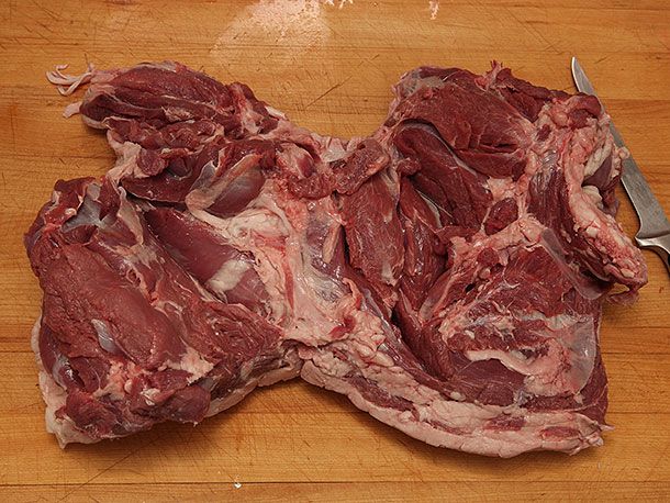 Butterflied boneless lamb leg resting on a cutting board next to a knife.