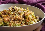 A bowl full of this salad, showing the varied textures of toasted breadcrumbs, thinly shaved raw Brussels sprouts, and crispy roasted ones, plus grated cheese, all lightly dressed in a creamy dressing.