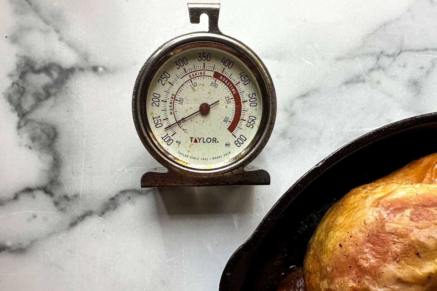 The Taylor analog oven thermometer on a marble surface next to a cast iron pan.