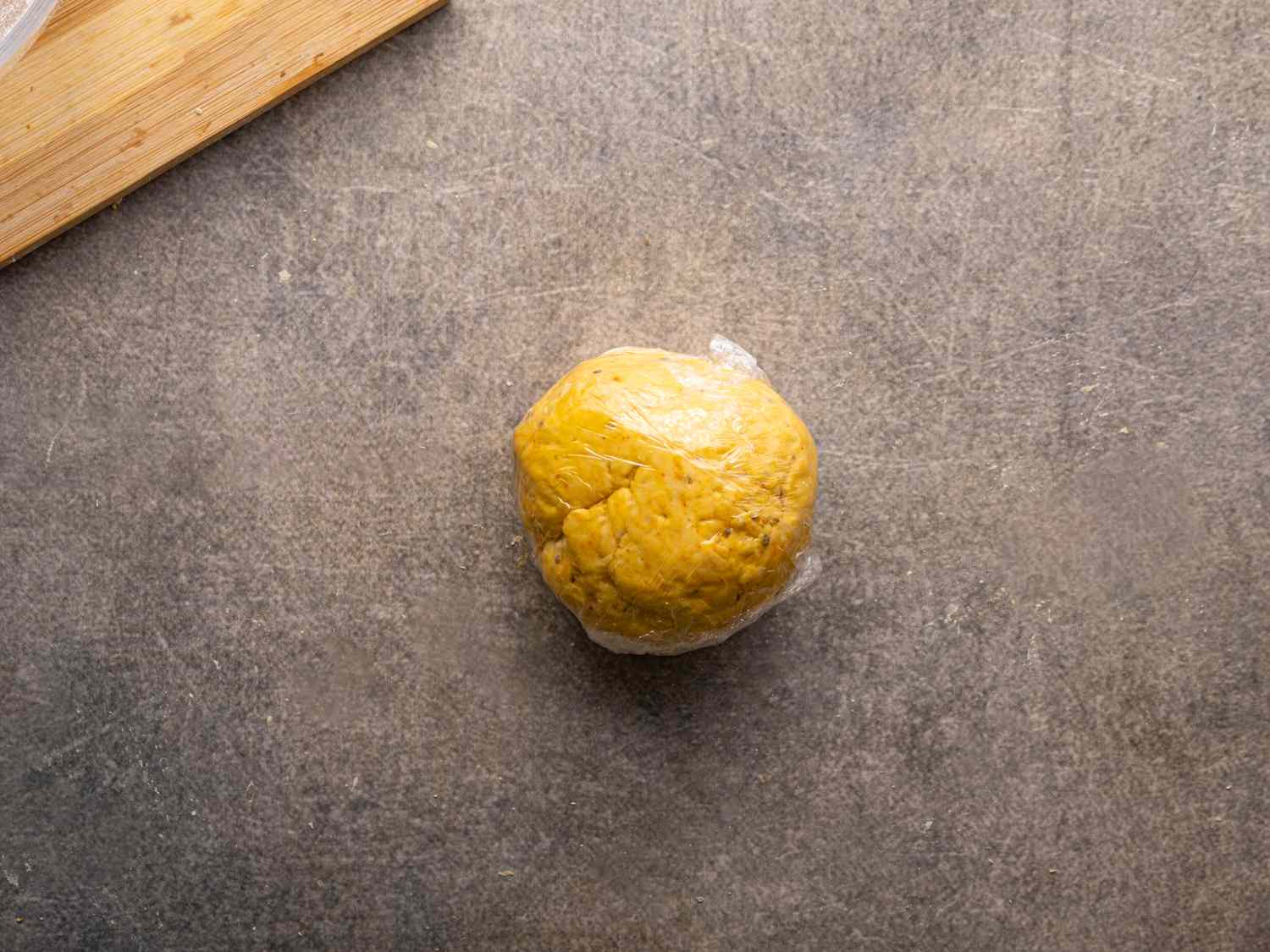 A ball of dough on a textured surface partially wrapped in plastic