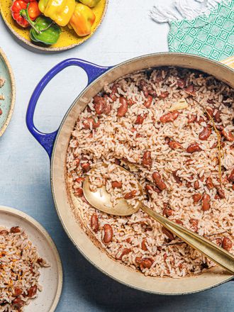 Overhead view of a pot of Jamaican rice and peas with a serving spoon, two serving plates and a green and yellow fabric