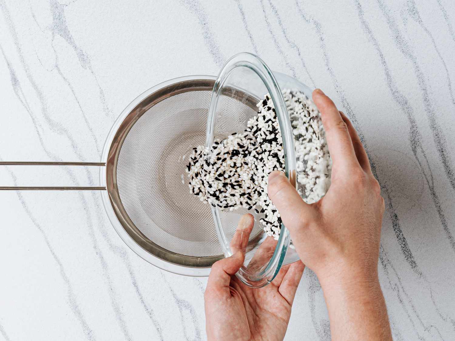 Long grain and purple rice poured through a fine--mesh strainer into a bowl 