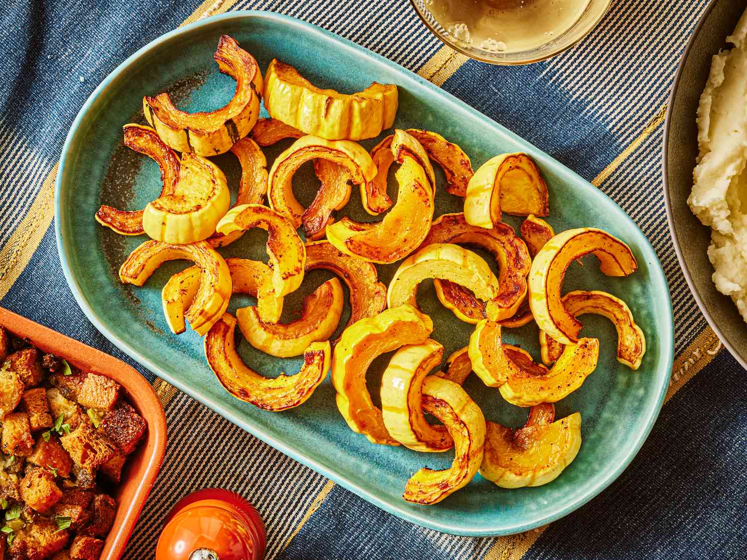 Roasted Delicata Squash on a turquoise platter, surrounded by thanksgiving dishes on a blue tablecloth