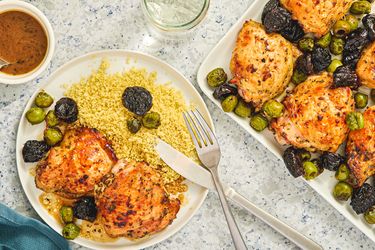 A dish of roasted chicken thighs with prunes olives and couscous on a plate and serving tray