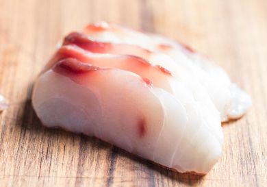Slices of sushi-grade raw fish on a wooden board.