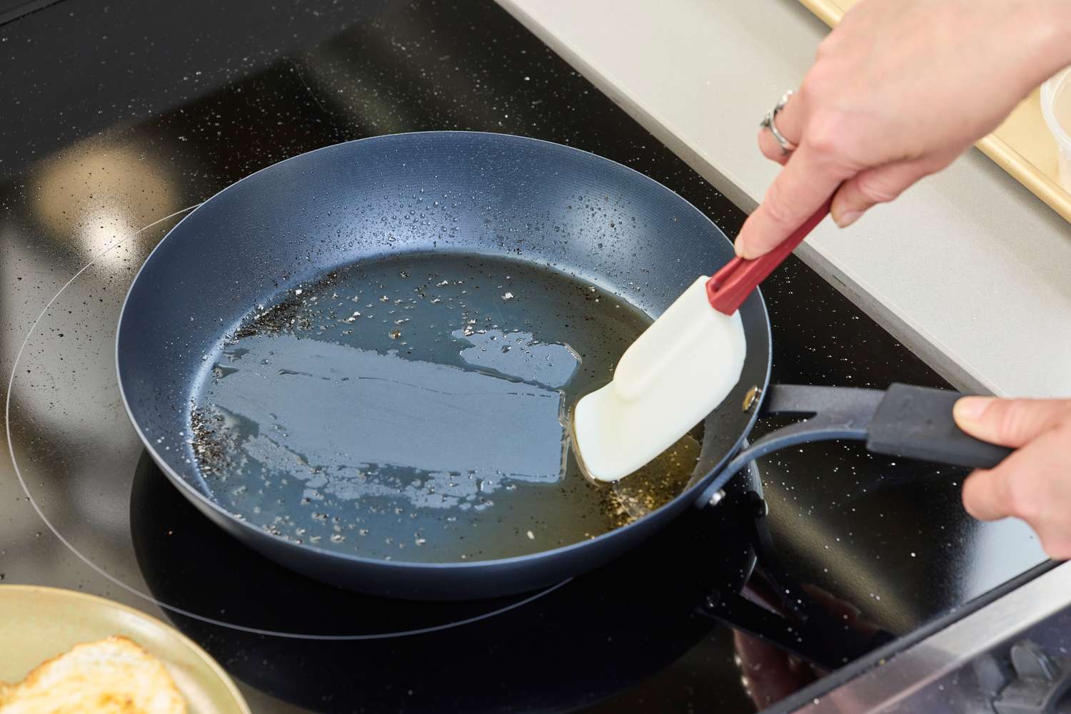 A person scrapes the bottom of the OXO Obsidian 10 Inch Pre-Seasoned Carbon Steel Frying Pan